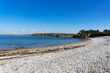 Sous un ciel bleu, la plage de galets de la presqu'île de Crozon s'étend sereinement.