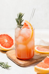 Grapefruit cocktail with rosemary garnish in a glass, served on a wooden cutting board. Vibrant, refreshing drink perfect for summer menu or cocktail recipes. Greyhound, lemonade, paloma, mocktail.