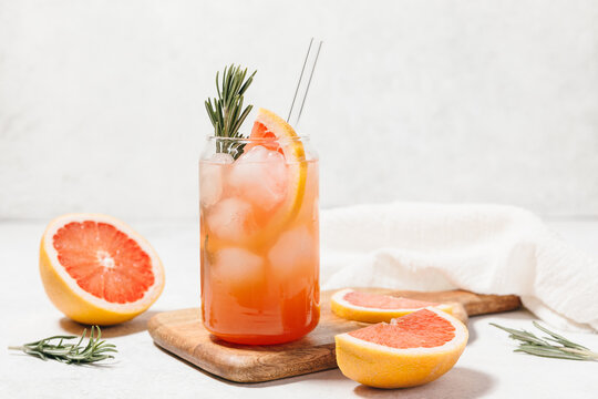 Grapefruit cocktail with rosemary garnish in a glass, served on a wooden cutting board. Vibrant, refreshing drink perfect for summer menu or cocktail recipes. Greyhound, lemonade, paloma, mocktail.