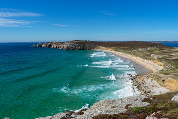 La plage de Pen Hat et la pointe du Toulinguet se détachent sous un ciel bleu, tandis que les eaux turquoises de la mer d'Iroise scintillent avec des touches d'écume blanche, créant une scène côtière 