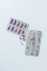 On a light background lie two blisters with capsules and lilac flowers inside. nearby are several capsules of different sizes and shapes and a lilac flower. Allergy medications