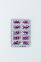 Lilac flowers in a blister instead of capsules are shot on a light background