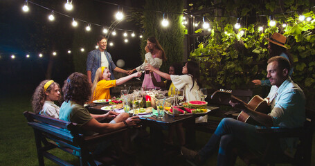 Joyful Caucasian couple dancing outdoor. African American girl talking while sitting. Mixed-races...