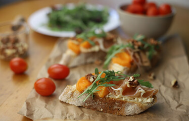 Italian appetizer bruschetta. Ready-made bruschetta made from bread, apricot, cheese and decorated with arugula and nuts lie on a wooden table and parchment. drinks for dinner nearby