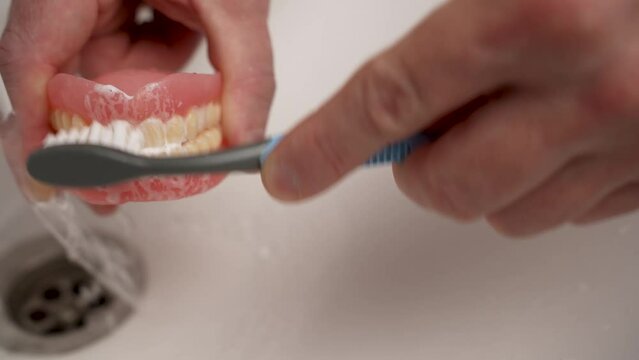 Close-up shot of cleaning dentures with toothbrush. Hand washing prosthesis teeth with brush and toothpaste