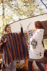 A couple of stylish ladies strike poses in their hippie ensembles near a trailer.
