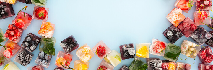 Frame of ice cubes with frozen berries and fruits and mint on blue background, banner