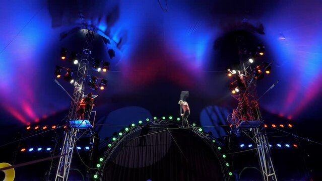 A circus show with tightrope walkers under the dome of the circus under the light of colorful spotlights and in smoke. A brave acrobat jumps on a rope on a rope under the dome of the circus.