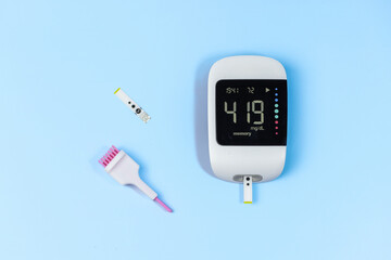 A blood glucose meter sits on a blue surface with a pink brush and a strip of test paper