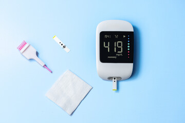 A glucose meter with a white screen and a pink and white handle. The meter is on a blue surface
