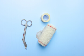 A pair of scissors and a roll of tape are on a blue surface. The scissors are silver and red, and...