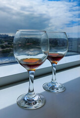 Two glasses on a long stem with drinks stand on the windowsill against the background of the city