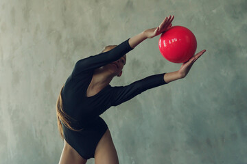 a young girl rhythmic gymnastics in a black bodysuit performs exercises with a ball