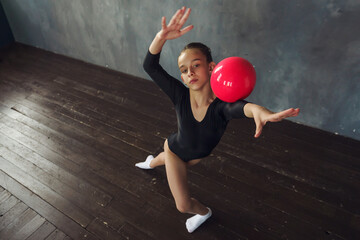 a young girl rhythmic gymnastics in a black bodysuit performs exercises with a ball