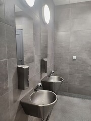 A stainless steel washbasin with an automatic faucet is mounted on a tiled wall in a public...