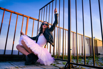 a ballerina in tutu sitting at the fence on the roof .at sunset in boots and a jacket