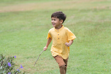 Happy little 4 year old Caucasian boy running in field with flowers garden smiling, laughing, sunny day. Cute child boy playing outdoors in summer in nature