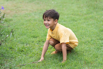 Happy little 4 year old Caucasian boy sitting in field playing hide and seek, smiling, laughing, sunny day. Cute child boy playing outdoors in summer in nature