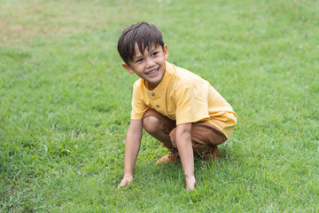 Happy little 4 year old Caucasian boy sitting in field playing hide and seek, smiling, laughing, sunny day. Cute child boy playing outdoors in summer in nature