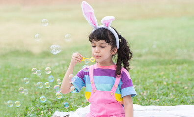 Happy 4 year old Caucasian little girl with bunny ears blowing soap bubbles in park, having fun,...