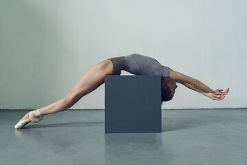 ballerina lies bent over on the cube gesturing with her legs