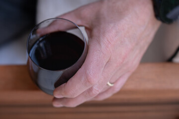 Close-up of an older male hand holding a stemless wine glass containing red wine outside