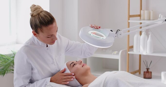 Doctor dermatologist or cosmetologist is providing a facial treatment for a woman patient at a beauty salon. The procedure of professional skincare and enhances the woman skin health and beauty.
