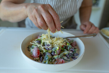 Woman sprinkling fresh grated gouda cheese over a salad