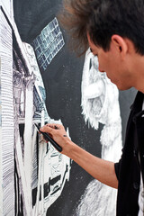 Young male painter passionately paints picture with black permanent marker for outdoor street exhibition using only black color, visual spectacle through expressive brush strokes