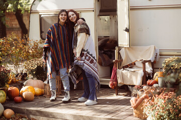 A pair of fashionable young women rock bohemian looks in front of a trailer.