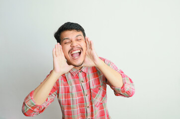 Young happy asian man announcing information with hands cup around mouth isolated on white studio...