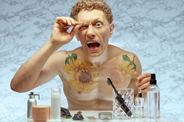 Funny image of shirtless emotional man taking care after his look, using tweezers for eyebrow hair...