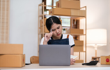 A small SME business owner feels tired while sitting on his home desk packing products into boxes.
