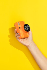 Hand holding retro film camera on yellow background