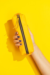 Hand holding yellow pencil case on yellow background
