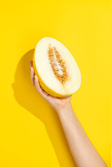Hand holding half melon on yellow background