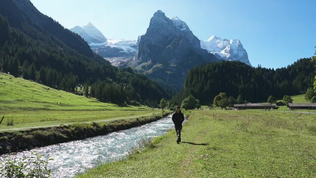 View of Rosenlaui with Wellhorn mountain and male tourist walking along Reichenbach river on sunny day