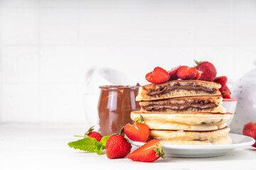 Stack of chocolate nutella filled pancakes. Sweet breakfast pancakes with chocolate sauce inside it, and fresh stawberries, on white kitchen table