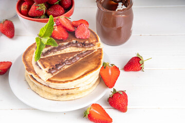 Stack of chocolate nutella filled pancakes. Sweet breakfast pancakes with chocolate sauce inside it, and fresh stawberries, on white kitchen table