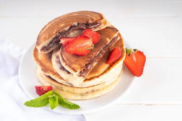 Stack of chocolate nutella filled pancakes. Sweet breakfast pancakes with chocolate sauce inside it, and fresh stawberries, on white kitchen table