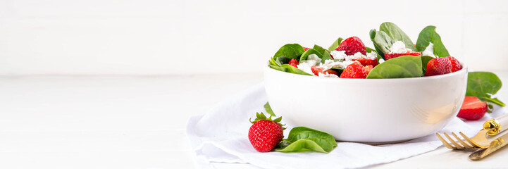 Spinach and strawberry summer salad with cottage cheese and balsamic sauce, fresh raw ripe fruit vegetable salad bowl, healthy diet food, on white kitchen table with cutlery