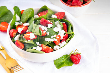 Spinach and strawberry summer salad with cottage cheese and balsamic sauce, fresh raw ripe fruit vegetable salad bowl, healthy diet food, on white kitchen table with cutlery