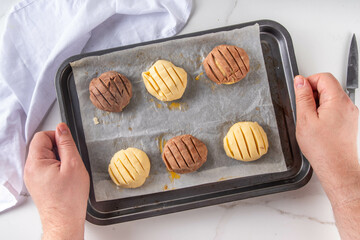 Cooking making mexican traditional conchas pastry, cookie or bread buns. Homemade preparation of conchas dessert pastry, on baking sheet with man hands in pic, top view copy space