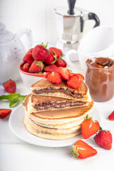 Stack of chocolate nutella filled pancakes. Sweet breakfast pancakes with chocolate sauce inside it, and fresh stawberries, on white kitchen table