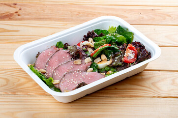 Salad with roast beef sous-vide. Healthy food. Takeaway food.  On a wooden background.