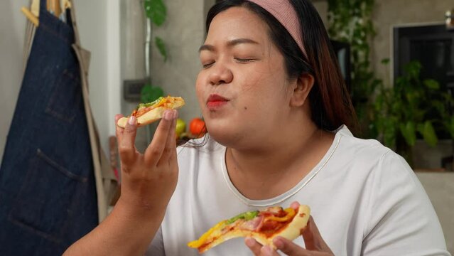 Happy Asian woman eating homemade pizza in home after baked pizza. Overweight women enjoy eating. Concept of binge eating disorder BED and Relaxing with Eating junk food and unhealthy foods.