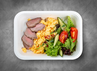 Scramble with veal and vegetables. Healthy diet. Takeaway food. Ecological packaging. Top view, on a gray background.