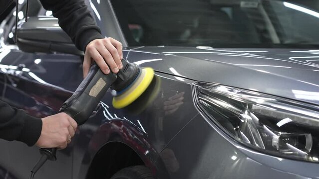 A mechanic polishes the surface of a gray car body. 
