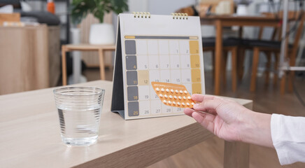Close-up, Young woman hands holding a birth control pill pack and a calendar to check when to take...