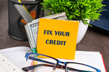 FIX YOUR CREDIT text written on a yellow sticker with dollars, on the desktop of a businessman, manager